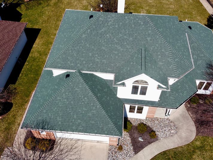 Green shingle roof surrounding a dormer above a landscaped front yard